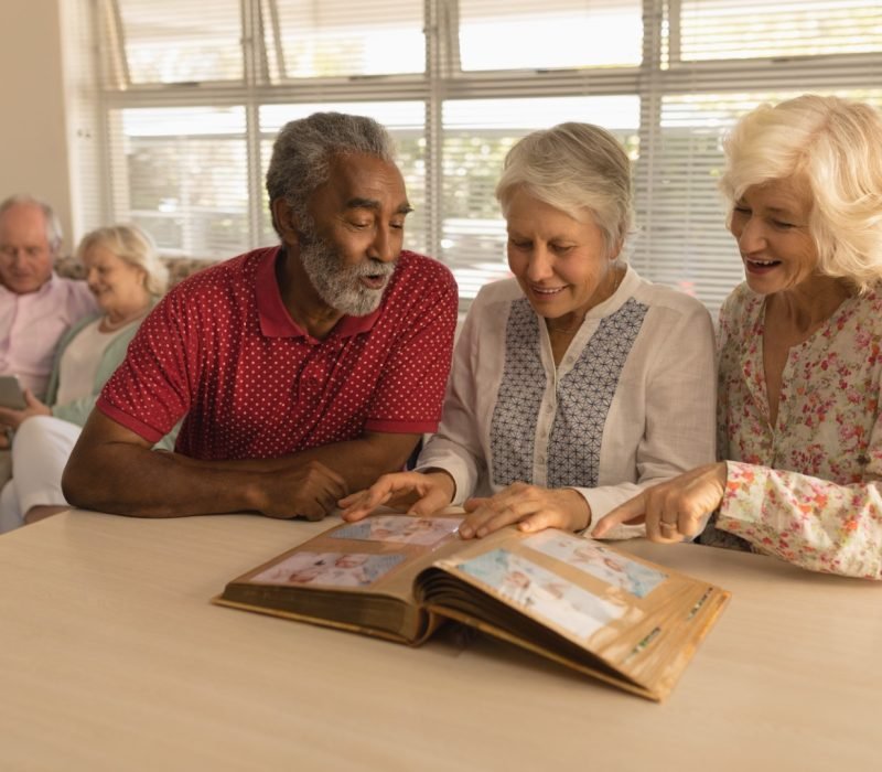 Front view of group of active senior people looking at photo album and showing a photo at nursing home