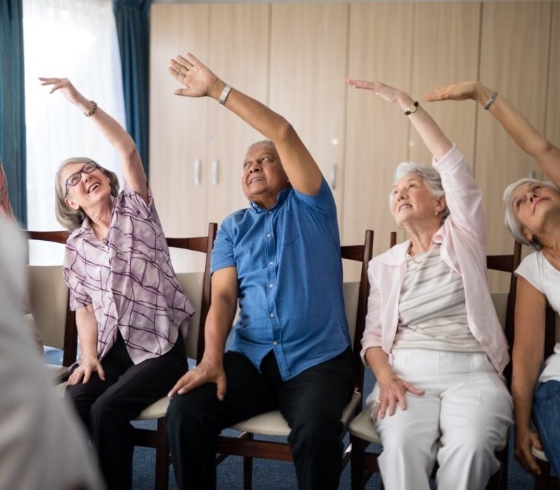 Smiling senior people stretching with female doctor at retirement home